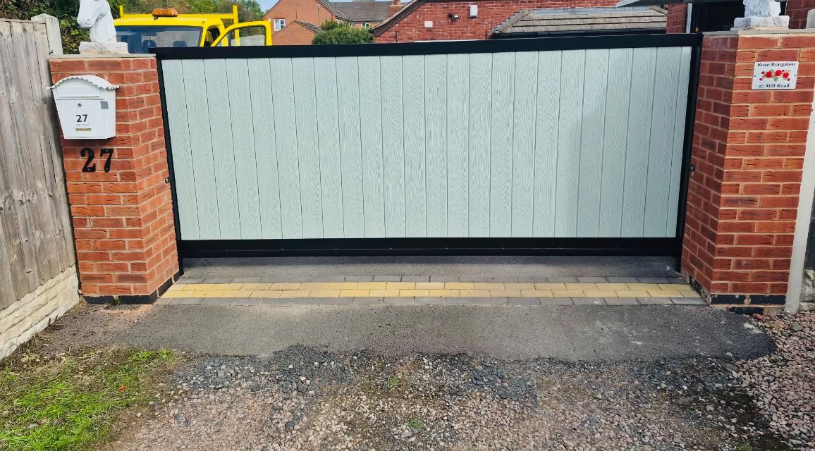 Sliding driveway gate with pale grey timber effect board infill between brick piers